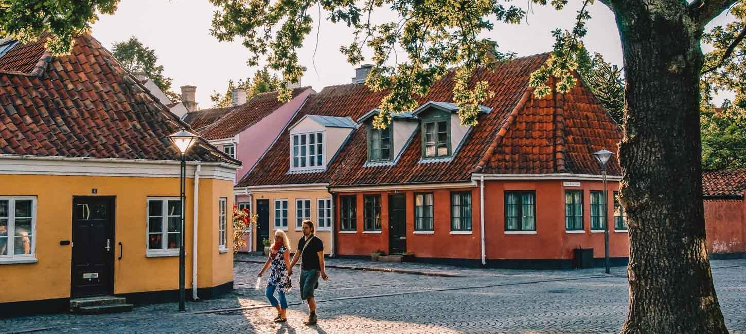 En kvinde og en mand går sammen foran tre farverige huse.