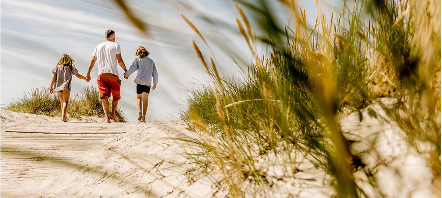 En familie går hånd i hånd på en strand.