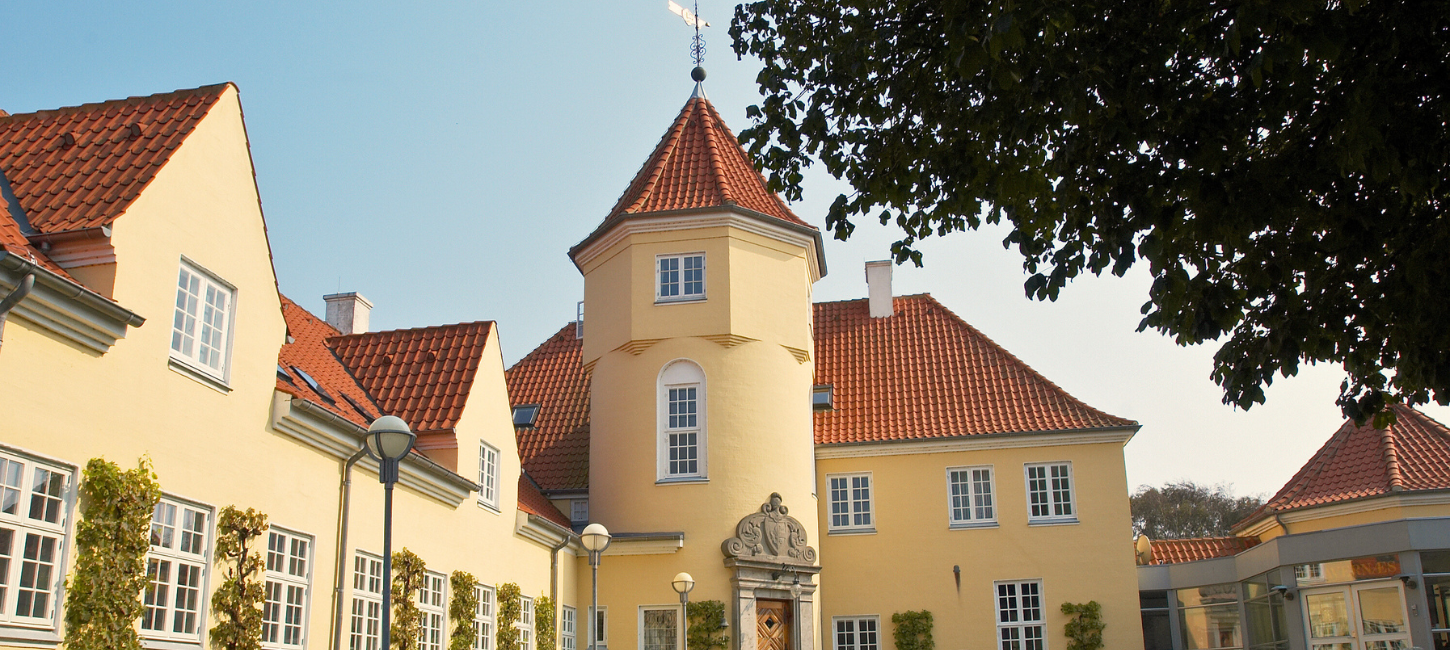 Et gult hotel med rødt tegltag og et tårn