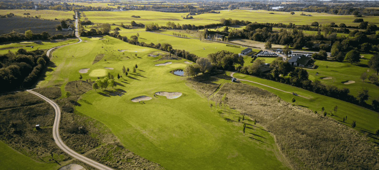 Luftfoto af golfbane med træer, stier og bunkers. 