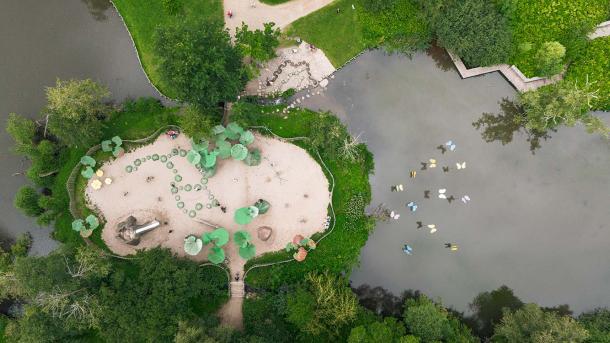 En legeplads på en ø midt i en sø med grønne omkransende træer og buskadser