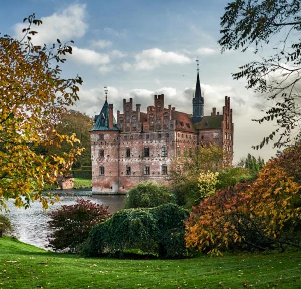 Egeskov Slot omgivet af træer og buske i efterårets farver.