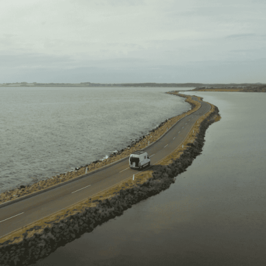 A white motorhome driving on a narrow dam with ocean to both sides