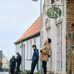 En mand læner sig op ad en husfacade med høretelefoner på ørerne og telefon i hånden 